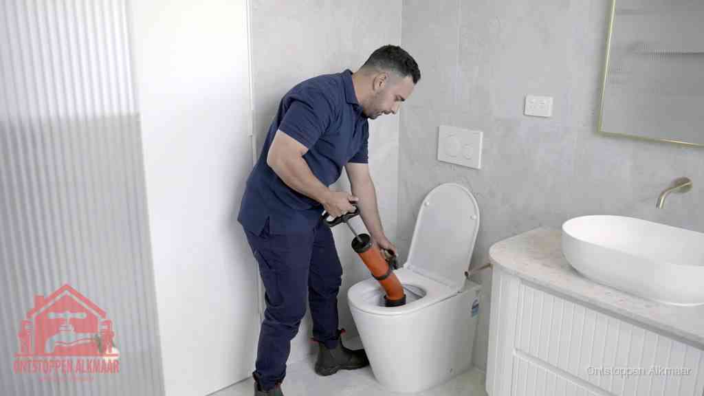 Een monteur buigt over een wandcloset en duwt met de hand een persluchtontstopper in de toiletpot om de verstopping handmatig los te maken in Alkmaar