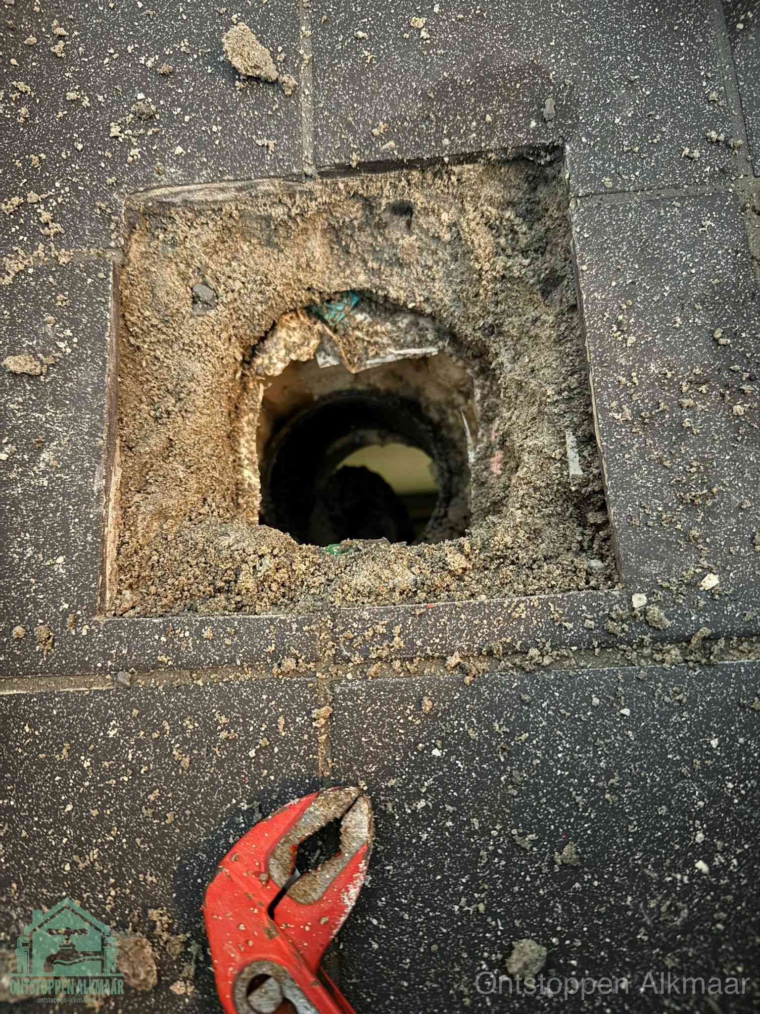 Een geopend rioolputje in een betontegelvloer met losgemaakt rooster en een zichtbare ronde afvoerbuis, het achterhalen waar de afvoerverstopping zit in Alkmaar
