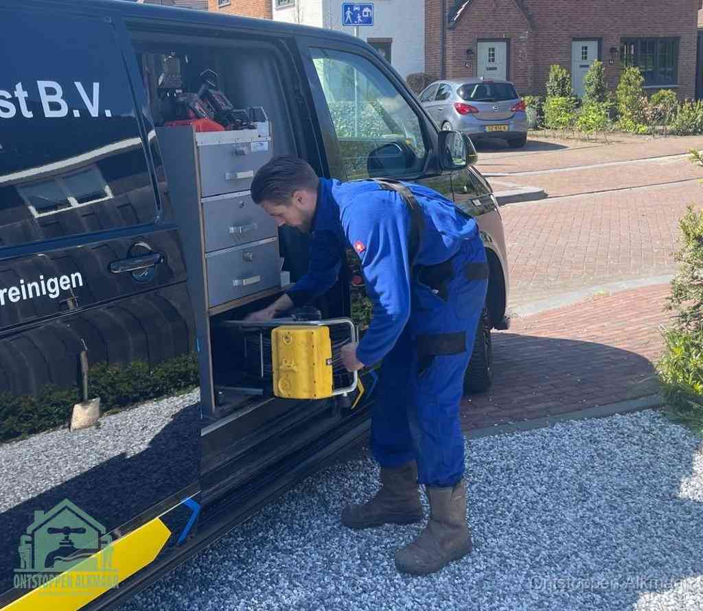 Een monteur pakt buiten op de oprit gereedschap uit de bedrijfsbus, het moment om een professional in te schakelen voor een verstopte afvoer in Alkmaar