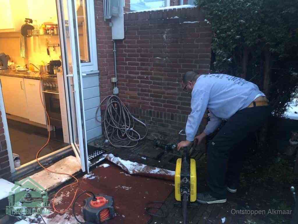 Een monteur werkt buiten bij een open riool-/grondput met een elektrische ontstoppingsmachine om een verborgen afvoerprobleem op te sporen in Alkmaar