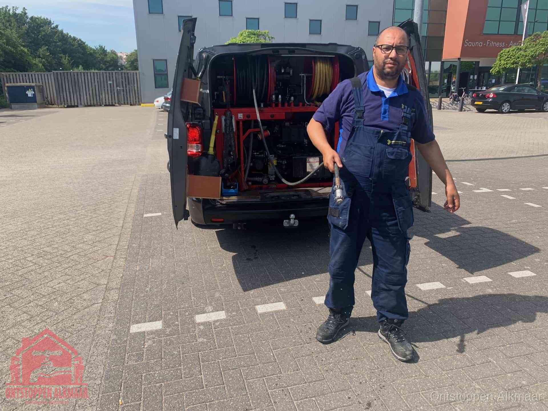 Een monteur bij zijn bestelbus met een hogedruk- en rioolreinigingsunit, klaar om de oorzaak van terugkerende wc-verstoppingen aan te pakken in Alkmaar